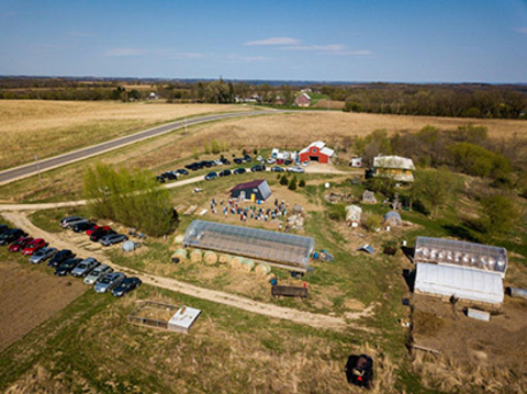 Aerial photo of a farm with a Deep Winter Greenhouse, other farm buildings and cars parked around the farm.