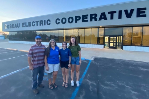 Four people standing in front of Roseau Electric Cooperative office building.