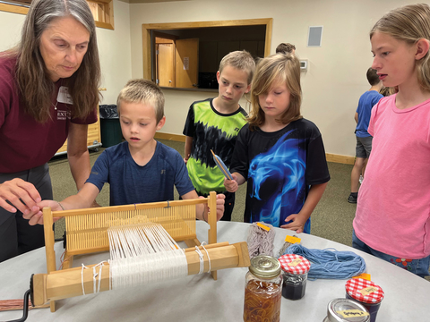 Master Gardener Sally Jacobsen shows a group of children how to use a weaving loom.
