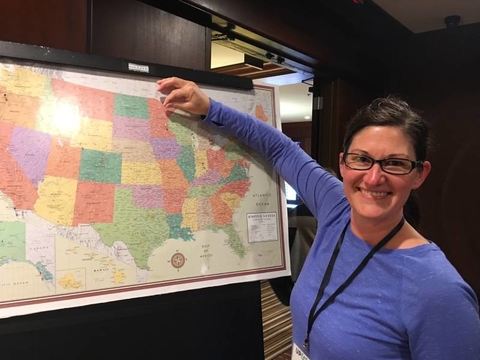 Sarah Verke standing in front of a wall map of the U.S. while putting a pin in Minnesota.