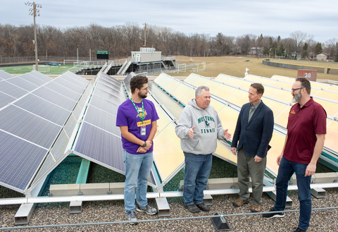 4 men in front of solar panels on a roof of a school bulding