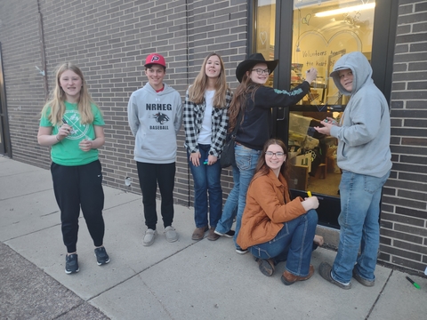 A group of youth standing on a sidewalk in front of a glass door.