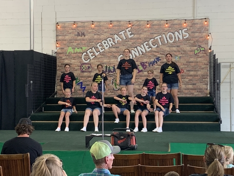 A group of youth wearing black t-shirts performing on a stage with a backdrop containing the words, "Celebrate connections."
