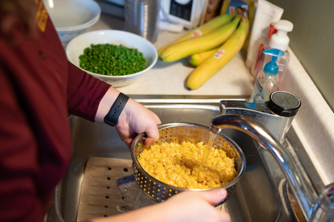 A person rinsing corn in a strainer