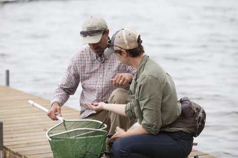 two people on a dock looking at something they found in fishing nets
