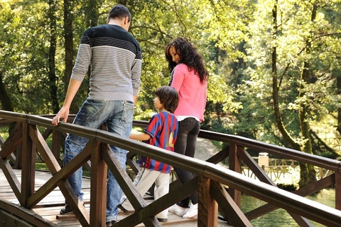 two parents and child walk over bridge in forest