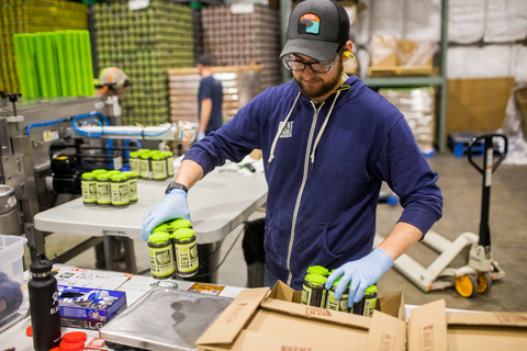 A man in a warehouse packs cans from Bent Paddle Brewing Co into boxes.