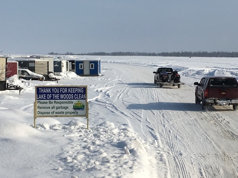 Trucks on a frozen lake and a sign that says to keep the lake clean. 