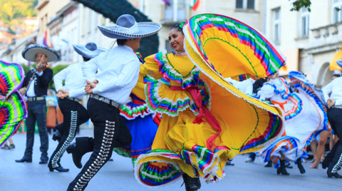 Two dancers in traditional Mexican dance clothing dancing at a cultural event.