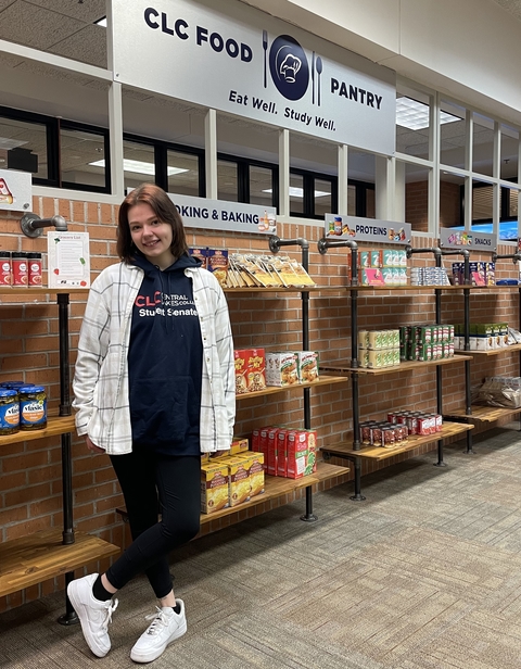 College student stands, smiling in front of shelves of food. Her shirt says "CLC Student Senate."