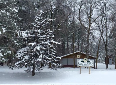 Snow covered ground and trees with a building in the background and a large Gary Pines sign in front of building.