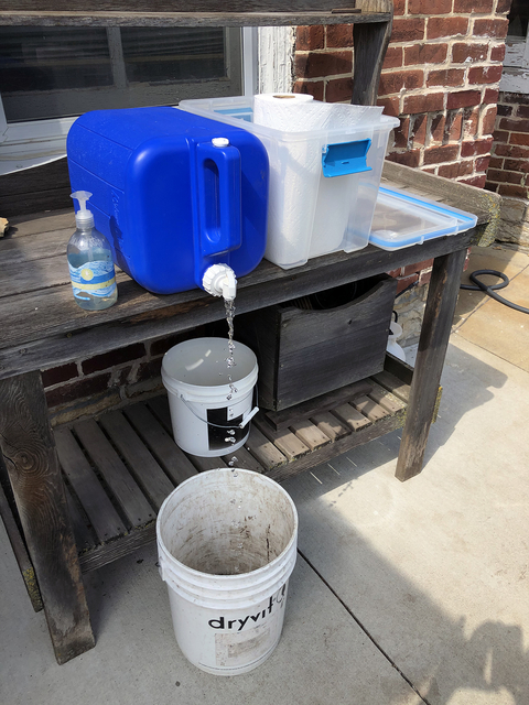 A blue jug of water, hand soap, and paper towels in a container on top of a potting bench.
