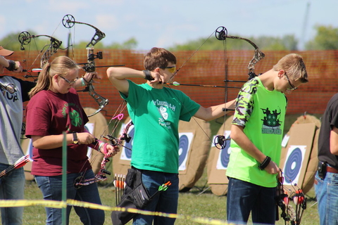 Three youth aiming archery equipment at targets.