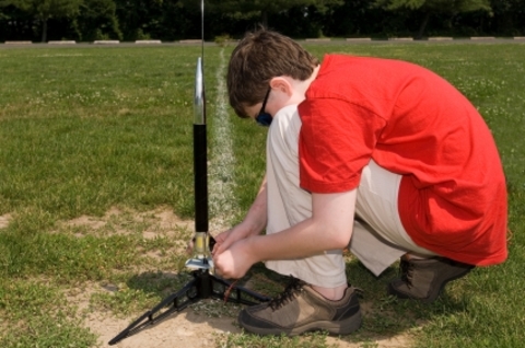 Boy in red shirt prepares his small black rocket for launch in grassy field