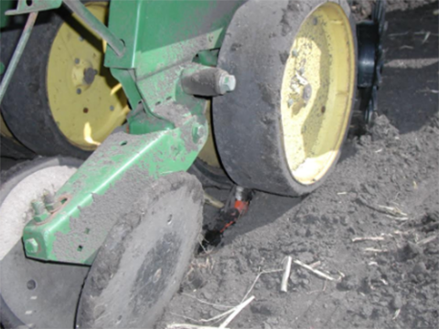 Close-up of a tractor wheel showing a tube applying fertilizer in a furrow in a field.