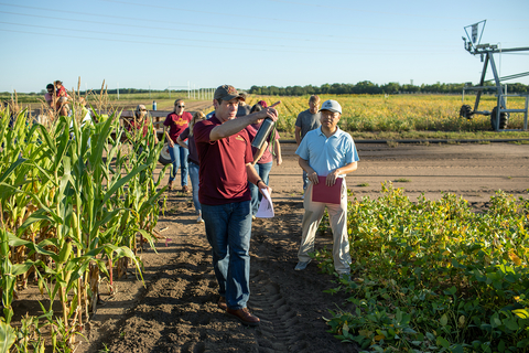 Man points in a southward direction in corn field while people follow him.