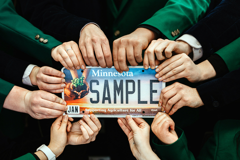 Minnesota license plate with the word "sample" and multiple hands holding it in a circle.