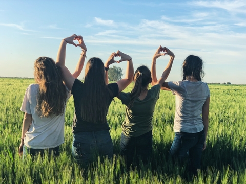 Girls in an open field making hearts with their hands.