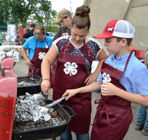 4 youth wearing 4-H aprons grilling meat 