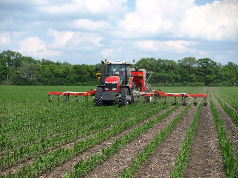 Red tractor applying Nitrogen to young green crop.