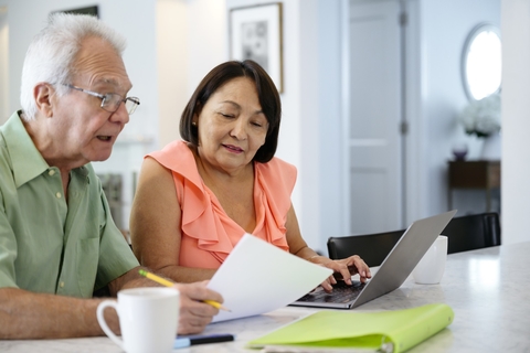Older adults fill out paperwork and work at a computer together. 
