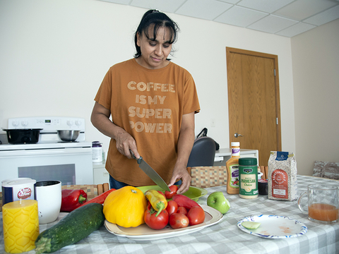 A person standing at a kitchen table cutting vegetables.