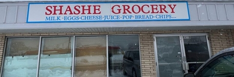 The front of Shashe Grocery featuring a sign advertising milk, eggs, cheese, juice, pop, bread and chips