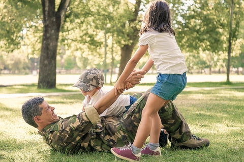 A soldier plays in the grass with his younger children. 