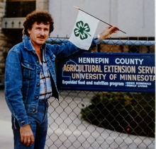 Bill Svendsgaard in 1976 in front of a Hennepin County sign and holding a small 4-H flag