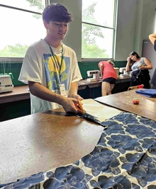 Participant cuts cloth while some behind him operate sewing machines