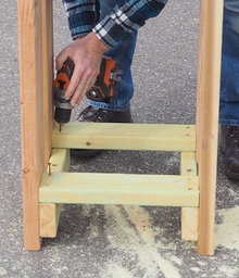Person using cordless drill to attach lower cross pieces.