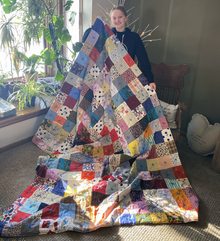 Teenager holds up a large colorful quilt that she made herself, her face beaming with pride
