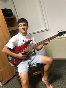 Youth holding guitar, sitting on a chair.