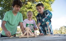 Girl and two boys playing with a wooden toy.