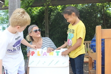 adult volunteer with a poster board that says PLANTS and each letter stands for something plants need, such as light and nutrients