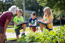 Master Gardener Jane Barton talks to students who are journaling in a garden.