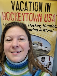 Katy Spoden in front of a sign that says vacation in Hockeytown, USA. 