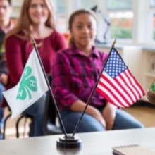 young girl sitting in a meeting with a 4-H and an American flag in the forefront