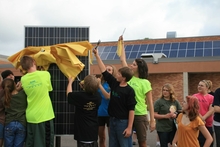 A group of student cutting a yellow ribbon from a new solar panel.