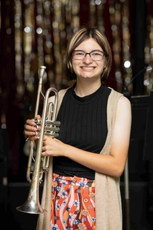 Participant in front of a glittery backdrop poses for the camera with her wind instrument