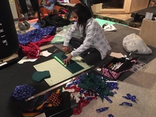 Person sitting on the floor cutting out material to make face masks.