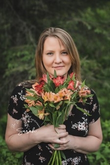 A portrait of Cynthia Baade holding a bouquet of orange and red flowers