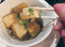 Chopstick reaching for a piece of fried tofu.