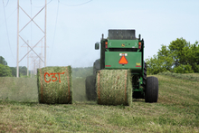 A round hay bale tied with twine is ejected from a baling machine.