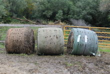 Three hay bales wrapped in twine, net wrap and B-wrap, respectively, outside near a fence.