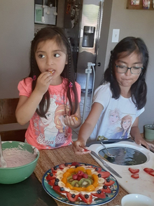 Two girls making fruit pizza at home.