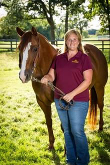Krishona Martinson standing with and holding reins of brown horse with white face
