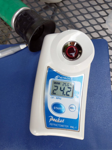 A refractometer measuring the sugar content of grape juice. The indicator reads 24.2.