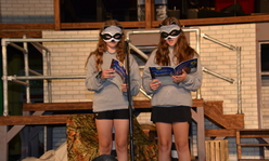 Two girls wearing raccoon costumes reading books on a stage.
