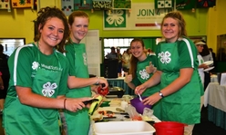 Four teens wearing green 4-H aprons cooking.